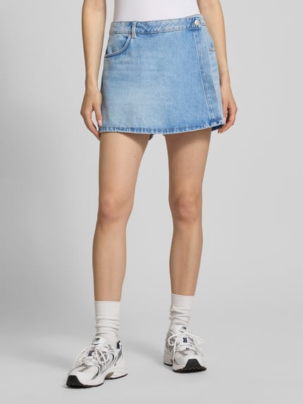 Frauenmodel trägt Jeans-Skort in hellblauer Waschung von REVIEW, Reine Baumwolle, Wickel-Optik, Eingrifftasche, Gesäßtaschen, Ganzkörperansicht von vorne.