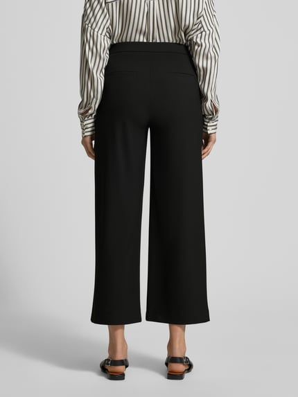 Frauenmodel trägt Wide Fit Schlupfhose mit Viskose-Anteil Modell 'Palina' von Raffaello Rossi in Schwarz mit Crêpe-Struktur, Ganzkörperansicht Rückansicht.