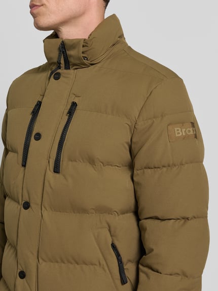 Männermodel trägt Steppjacke mit Kapuze von BRAX in Unifarbe, Logo-Patch, Reißverschlusstaschen, Detailaufnahme Oberkörper.