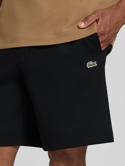 Männermodel trägt Regular Fit Sweatshorts aus Baumwoll-Mix von Lacoste in Schwarz mit glatter Textur, Nahaufnahme Oberschenkel, Herren Sweatshorts.