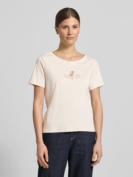 Vrouwenmodel draagt T-shirt met motiefprint en strass-steentjes van monari, puur katoen, recht model, ronde hals, ruglengte maat 36: 57 cm, Ganzkörperansicht von vorne.