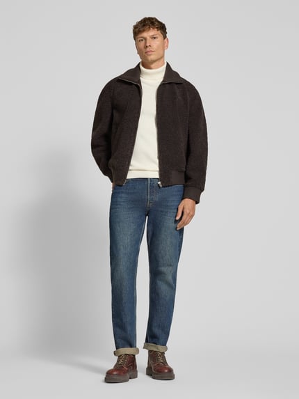 Männermodel trägt Jacke mit Stehkragen und Reißverschluss Modell 'GRALON' von DRYKORN aus Teddyfell, frontale Ganzkörperansicht.