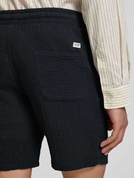 Mannenmodel draagt donkere short met structuurpatroon, steekzakken en elastische band, model 'AIDEN' van Jack & Jones, detailopname rug. Materiaalmix met katoen, straight fit, bandwijdte maat M 40 cm, binnenbeenlengte 21 cm.