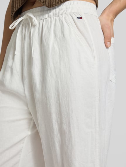 Vrouwenmodel draagt Weite Hose aus Leinen-Mix mit Tunnelzug van Tommy Jeans in tweekleurige look, loose fit, gestikt logo, boord met tunnelkoord, zij-steekzakken, opgestikte achterzakken, linnenmix. Nahaufnahme onderlichaam.