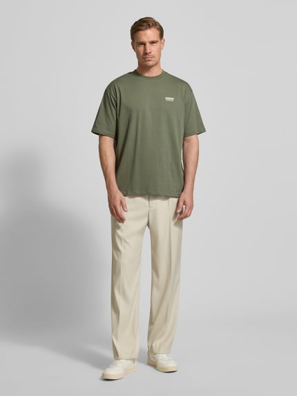 Männermodel trägt T-Shirt mit Label-Print Modell 'Baine' von WOODBIRD in Olive, Regular Fit aus Bio-Baumwolle, Ganzkörperansicht von vorne.