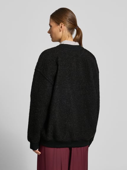 Frauenmodel trägt Cardigan mit Logo-Patch von Lacoste in Schwarz, Melange-Strickoptik, Strukturmuster, Ganzkörperansicht Rückansicht.