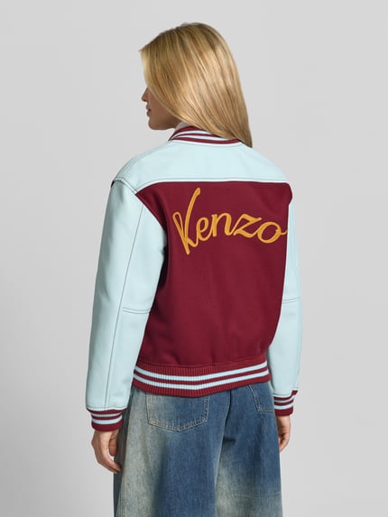 Frauenmodel trägt College-Jacke mit Logo-Patch von Kenzo in Two Tone Optik, Strukturmuster, Kontraststreifen, Rückansicht, Ganzkörperansicht.