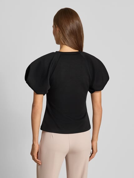 Vrouwenmodel draagt Bluse mit Ballonärmeln van Rinascimento in zwart, Materiaalmix met stretch, getailleerde pasvorm, ruglengte 55 cm, mouwlengte 27 cm, ronde hals, ballonmouwen, Ganzkörperansicht Rückansicht.