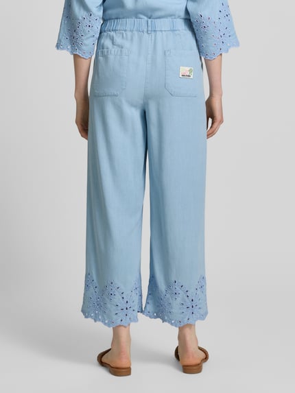 Frauenmodel trägt Hose mit Lochstickerei und französischen Eingrifftaschen von Smith and Soul aus Lyocell in Hellblau, Ganzkörperansicht Rückansicht. Wide-Leg-Fit, elastischer Bund mit Knopf-Reißverschluss, Innenbeinlänge 67 cm bei Größe S.