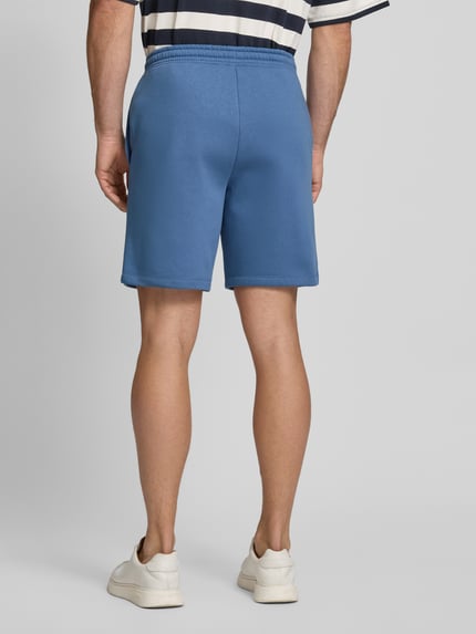 Männermodel trägt Sweatshorts mit Logo und elastischem Bund von GAP aus Baumwoll-Mix in Blau, Regular-Fit, Eingrifftaschen, Ganzkörperansicht Rückansicht.
