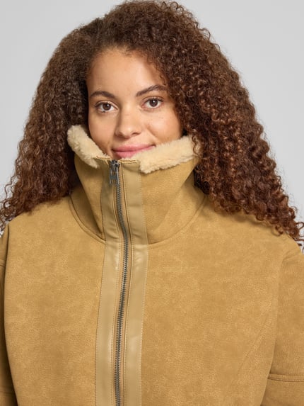 Frauenmodel trägt Kunstlederjacke mit Teddykragen von Edited, beige Farbe, glatte und flauschige Texturen, Nahaufnahme Oberkörper; Rückenlänge bei Größe S: 66 cm, Schulterbreite: 58 cm, Brustweite: 64 cm, Ärmellänge: 54 cm.
