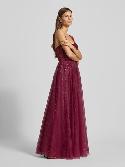 Modelka kobieca nosi szimmerndes Abendkleid in semitransparenter Optik von Hey Kyla, długa suknia z tiulu w kolorze bordowym, krój taliowany, widok całej sylwetki z boku.
