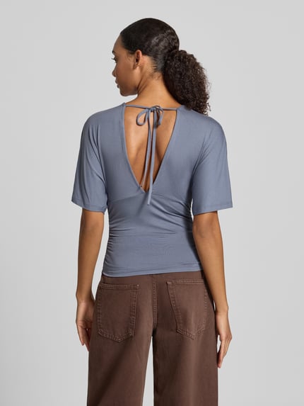 Frauenmodel trägt Bluse aus Viskose-Mix mit V-Ausschnitt von Gina Tricot in Blau, taillierte Passform, Rückenansicht, Ganzkörperansicht von hinten.