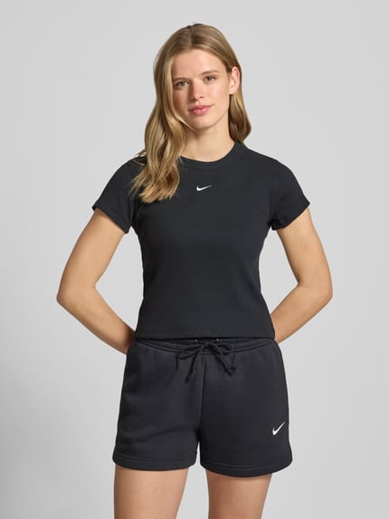 Frauenmodel trägt Cropped T-Shirt in Ripp-Optik mit Logo von Nike aus Baumwoll-Elasthan-Mix, schwarzer Farbton, Rundhalsausschnitt, Rückenlänge bei Größe S 48 cm, Ganzkörperansicht von vorne.