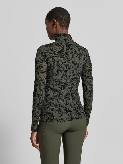 Frauenmodel trägt Longsleeve aus Mesh von Marc Cain im taillierten Schnitt mit Rollkragen, florales Muster, Ganzkörperansicht Rückansicht. Material-Mix mit Viskose-Anteil, Rückenlänge 60 cm bei Größe 36.