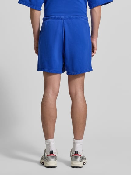 Männermodel trägt Shorts mit Logo Modell 'PLIZZY' von American Vintage in Blau aus Reine Baumwolle, Relaxed-Fit, Ganzkörperansicht Rückansicht.