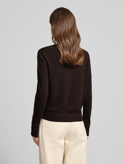Frauenmodel trägt Strickjacke aus reinem Kaschmir mit durchgängiger Knopfleiste von Christian Berg Woman in Dunkelbraun, Regular Fit, gerippte Abschlüsse, langärmliges Design, gerippte Blende, kombiniert mit heller Hose, Ganzkörperansicht Rückansicht.