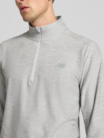Männermodel trägt Regular Fit Sweatshirt mit Troyer-Kragen von New Balance, hellgrauer Ton, glatte Textur, Logo-Print, Nahaufnahme Oberkörper.