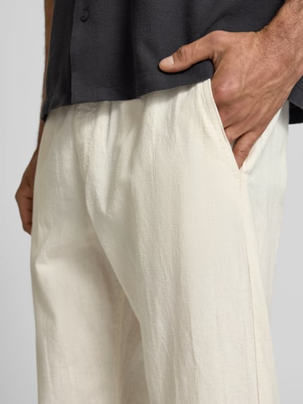 Männermodel trägt Relaxed Fit Hose aus Baumwoll-Leinen-Mix Modell 'KANE' von Jack & Jones in Creme mit Tunnelzug, Gesäßtasche, Nahaufnahme Oberkörper. Bundweite 41 cm, Innenbeinlänge 77 cm.