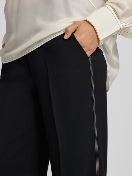 Vrouwenmodel draagt Hose met wijd been en steekzakken van Marc Cain met persplooien, galonstrepen, elastische band, detailopname.