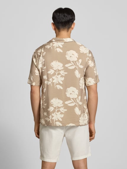 Männermodel trägt Regular Fit Freizeithemd aus Viskose-Mix von REVIEW in Beige mit weißem Blumenmuster und strukturierter Oberfläche, Ganzkörperansicht Rückansicht. Rückenlänge bei Größe M: 74 cm, Schulterbreite bei Größe M: 54 cm, Ärmellänge bei Größe M: 30 cm, Reverskragen, 1/2-Arm, Knopfleiste.