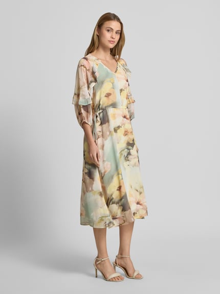 Frauenmodel trägt Midikleid mit V-Ausschnitt von Soyaconcept, Leicht taillierte Passform, Midilänge, 3/4-Arm, Rüschenbesatz, Rückenlänge 128 cm, Brustweite 40 cm, Ärmellänge 42 cm, pastellfarbene, fließende Textur, florales Muster, Ganzkörperansicht von vorne.