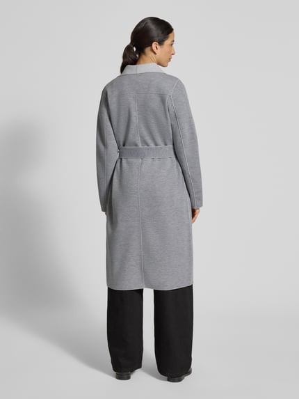 Frauenmodel trägt Relaxed Fit Mantel mit Viskose-Anteil Modell 'Juice' von Vila in Hellgrau, Schalkragen, abnehmbarer Stoffgürtel, Ganzkörperansicht Rückansicht.