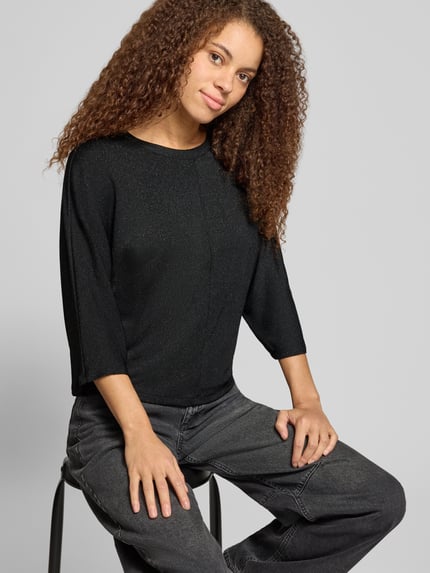 Frauenmodel trägt Langarmshirt mit shimmender Optik von ONLY in Schwarz mit Rundhals, 3/4-Arm, abgerundetem Saum und Jerseystruktur, Ganzkörperansicht von vorne.