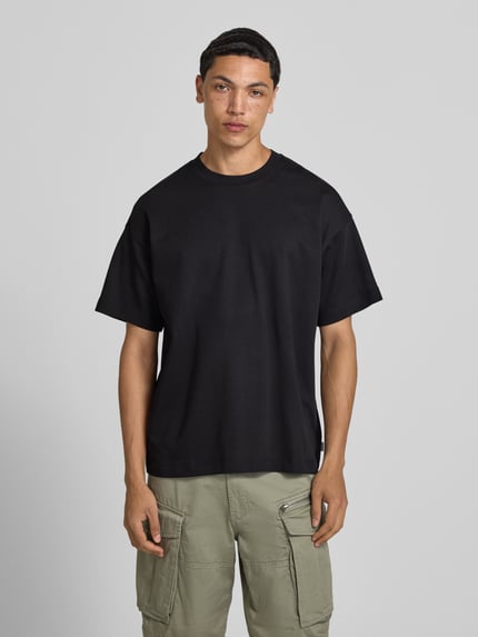 Männermodel trägt Jack & Jones Herren T-Shirt mit Baumwoll-Mix und Stretch-Anteil, Relaxed-Fit, Modell 'BARRON', schwarzer Stoff, Ganzkörperansicht von vorne.