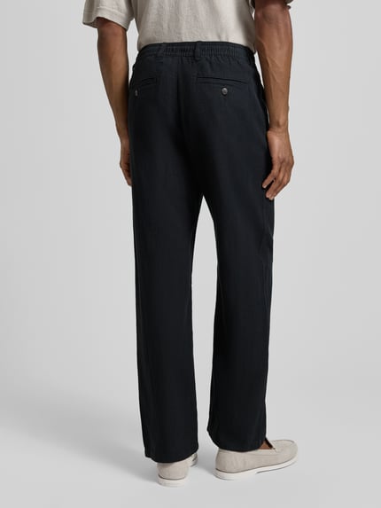 Männermodel trägt Loose Fit Leinenhose mit Tunnelzug Modell 'BRODY' von Selected Homme, Optik: Unifarben, Flammgarnstruktur, Bio-Baumwoll-Leinen-Mix, Gesäßtaschen mit Knopf, Materialverarbeitung, Ganzkörperansicht Rückansicht.