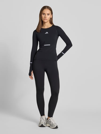 Vrouwenmodel draagt zwart slim fit shirt met lange mouwen met reflecterende details model 'adi365' van adidas Training, geheelvooraanzicht.