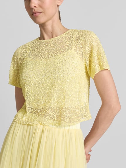 Modelka nosi Cropped T-Shirt mit Pailletten von LACE & BEADS, żółta siateczka z cekinami, okrągły dekolt, długość tyłu S: 41 cm, zbliżenie górnej części ciała