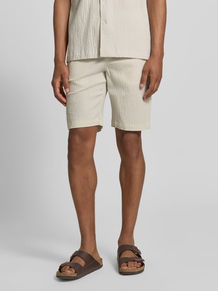 Männermodel trägt Shorts mit elastischem Bund und Strukturmuster von Lindbergh im Baumwoll-Mix mit Stretch-Anteil, Loose-Fit, Eingrifftaschen, Farbe Beige, Bundweite 42 cm, Innenbeinlänge 25 cm, Ganzkörperansicht von vorne.