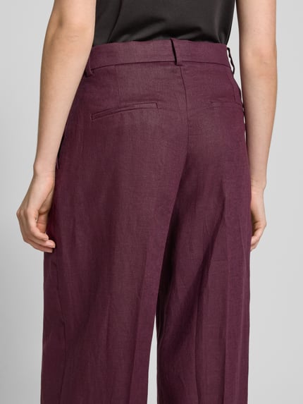 Frauenmodel trägt Straight Fit Leinenhose mit Bügelfalten Modell 'Tempoli' von Mango in dunklem Violett, Reine Leinen, Ganzkörperansicht Rückansicht.