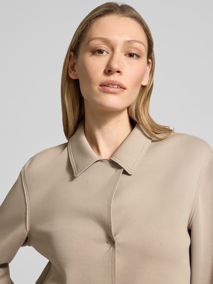 Frauenmodel trägt Blazer mit Kentkragen und aufgesetzten Pattentaschen von WHITE LABEL, glatter beigefarbener Baumwoll-Mix, Nahaufnahme Oberkörper. Gerader Schnitt mit Stretch-Anteil, verdeckter Verschluss, sichtbare Struktur, Damenmode.