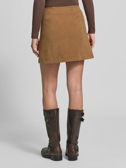 Frauenmodel trägt Regular Fit Mini-Rock aus Baumwoll-Mix in Cord-Optik von ARMEDANGELS, warme Braunfarbe, Ganzkörperansicht Rückansicht. Damen Mini-Rock von ARMEDANGELS
