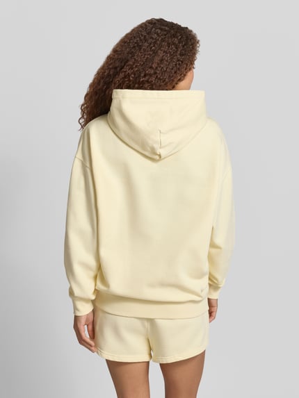 Frauenmodel trägt Oversized Hoodie mit Label-Stitching Modell 'CLARITA' von Pegador aus Baumwoll-Mix in Hellgelb, Känguru-Tasche, Ganzkörperansicht Rückansicht.