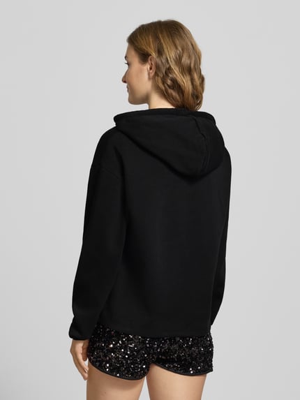 Vrouwenmodel draagt Regular Fit Hoodie uit katoenmix model 'CHILLI' van Pieces, effen zwart, label stitching, capuchon, sweattextuur, lange mouw, geribde zoom, rugaanzicht.