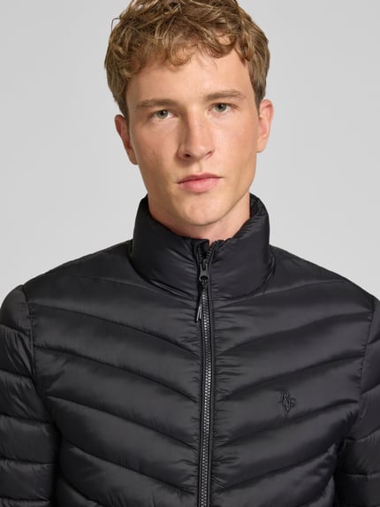 Männermodel trägt Regular Fit Steppjacke mit Logo-Stickerei von REVIEW in Schwarz, gesteppt, Stehkragen, Nahaufnahme Oberkörper.