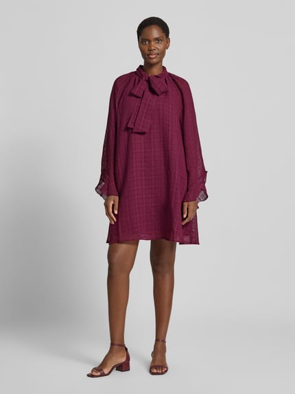 Vrouwenmodel draagt mini-jurk met strik, Loose fit in donkerrood met semitransparante mouwen, onderjurk, Model 'LIANA' van YAS, ruglengte 88 cm, borstwijdte 47 cm, mouwlengte 46 cm, geheel vooraanzicht