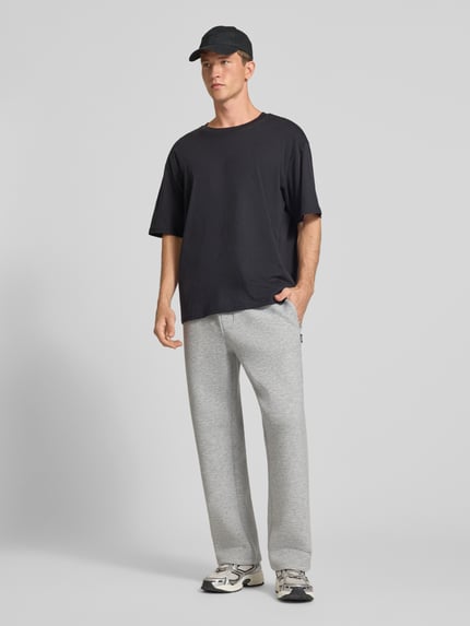 Männermodel trägt Regular Fit Sweatpants aus Material-Mix Modell 'BILL LEGACY' von JACK & JONES in Grau, Baumwollstruktur, Ganzkörperansicht von vorne, Herren Sweatpants, Eingrifftaschen, elastischer Bund mit Tunnelzug, Innenbeinlänge bei Größe M 77 cm.