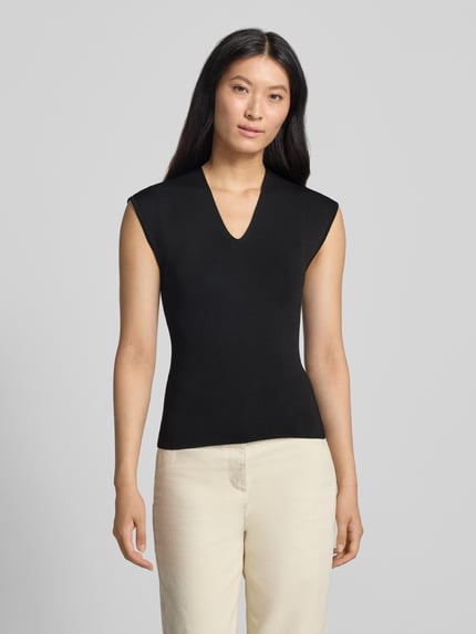 Frauenmodel trägt Stricktop mit V-Ausschnitt Modell 'CANELONS' von MANGO, taillierter Schnitt in Schwarz, feine Textur, Ganzkörperansicht von vorne.
