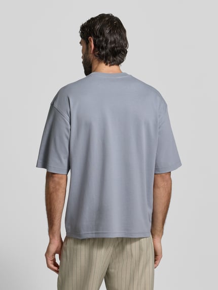 Männermodel trägt Relaxed Fit T-Shirt aus reiner Bio-Baumwolle von JAKE*S STUDIO MEN in Hellgrau mit Rundhalsausschnitt, Ganzkörperansicht Rückansicht.