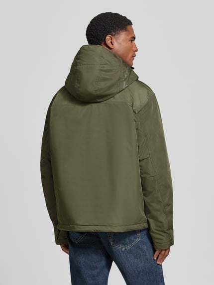 Männermodel trägt Jacke mit Kapuze und kurzem Reißverschluss von Napapijri in Olivgrün, strukturierter Stoff, Ganzkörperansicht Rückansicht, Modell 'RAINFOREST NEXT', gerader Schnitt, Kapuze mit Tunnelzug und Kordelstoppern, Pattentasche, Label-Patches.
