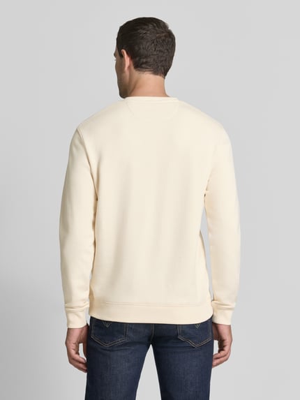 Męski model nosi Sweatshirt mit Label-Badge und Rundhalsausschnitt od Scotch & Soda, bawełna, krój regular fit, długość tyłu 71 cm, długość rękawów 68 cm, widok całej sylwetki z tyłu.