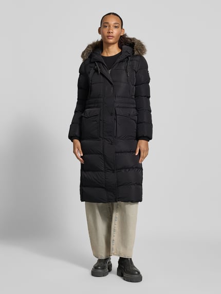 Frauenmodel trägt schwarzen Steppmantel mit Pattentaschen von Superdry, Kapuze mit Kunstfell, Regular Fit, Ganzkörperansicht von vorne.