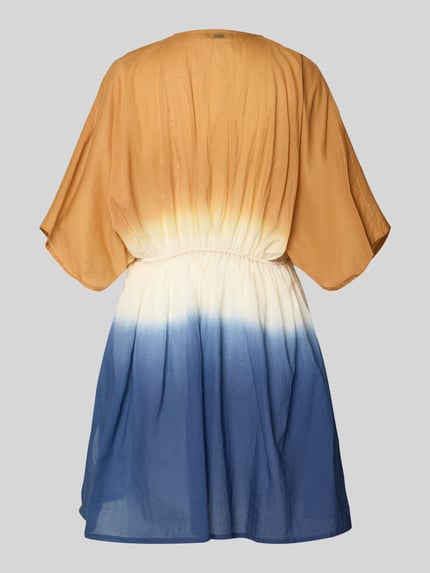 Vrouwenmodel draagt Strandkleid mit V-Ausschnitt Modell 'Mundoly' van Barts uit puur katoen in getailleerd model als mini-jurk met plooien en labeldetail achterzijde, kleurverloop in oker, crème en blauw, Ganzkörperansicht Rückansicht.