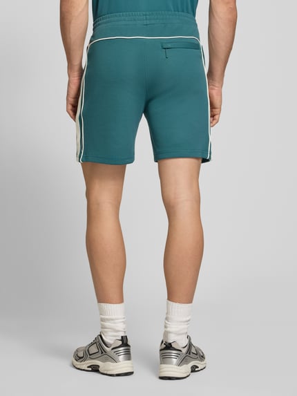 Männermodel trägt Shorts mit Logo-Stitching Modell 'EGEO' von SERGIO TACCHINI in Türkis mit weißen Streifen, lockerer Schnitt, Ganzkörperansicht Rückansicht.