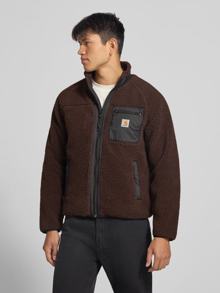 Männermodel trägt braune Teddyjacke mit Brusttasche Modell 'PRENTIS LINER' von Carhartt Work In Progress, Reißverschluss, Label-Patch, Ganzkörperansicht von vorne, Herrenjacke Regular Fit, Stehkragen, seitliche Taschen.