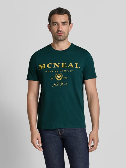 Männermodel trägt T-Shirt mit Label-Print und Rundhalsausschnitt von MCNEAL in Dunkelgrün, Reine Baumwolle, Regular-Fit, Ganzkörperansicht von vorne. Rückenlänge bei Größe M: 68 cm.